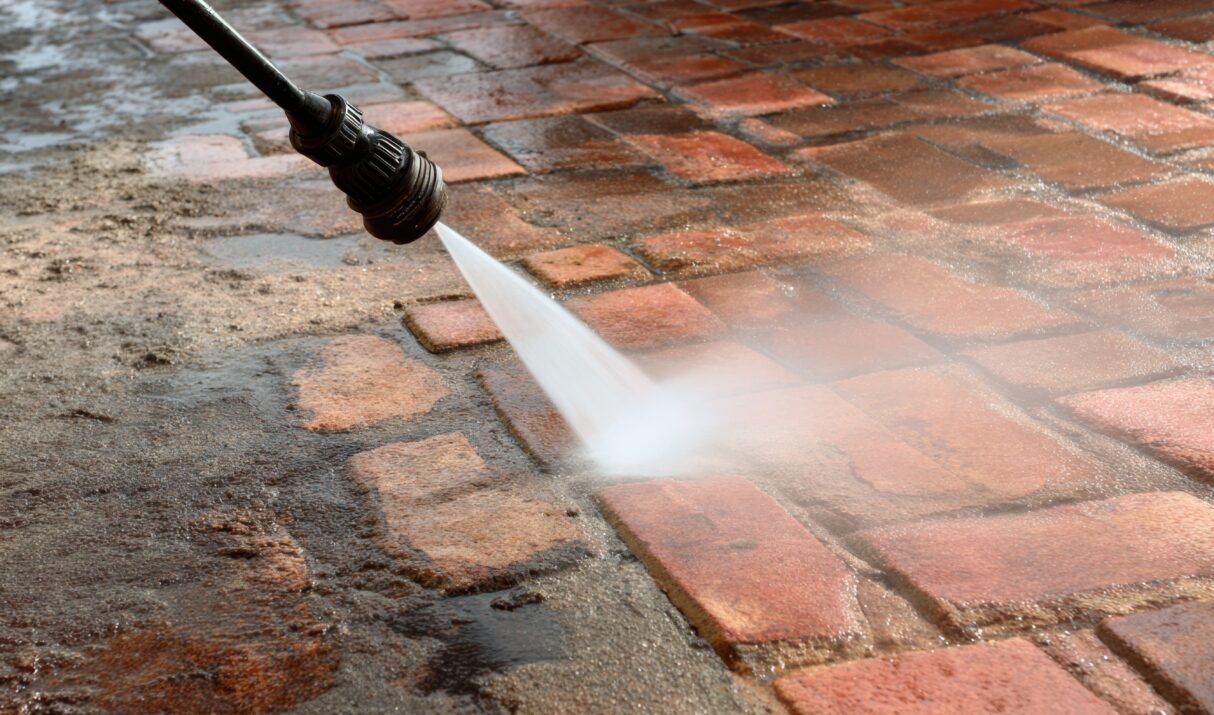 Close-up of a high-pressure water spray cleaning dirt and grime off a brick pavement outdoors