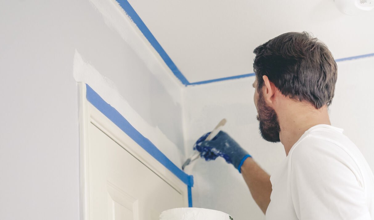 Close up of painter hands with gloves painting the wall edge by door frame.
