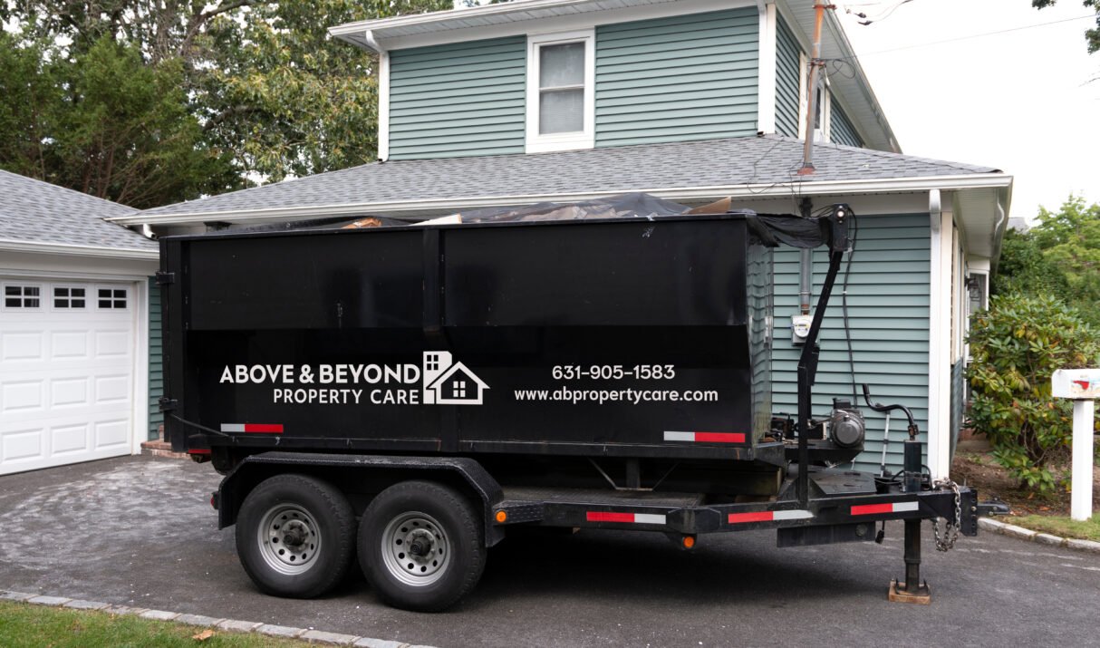 A contractors dumpster is on a trailer for easy hauling in their customers driveway.