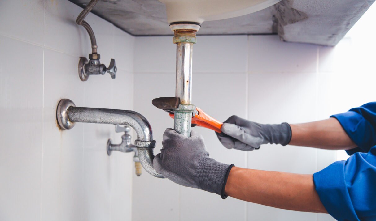 Technician plumber using a wrench to repair a water pipe under the sink. Concept of maintenance, fix water plumbing leaks, replace the kitchen sink drain, cleaning clogged pipes is dirty or rusty.